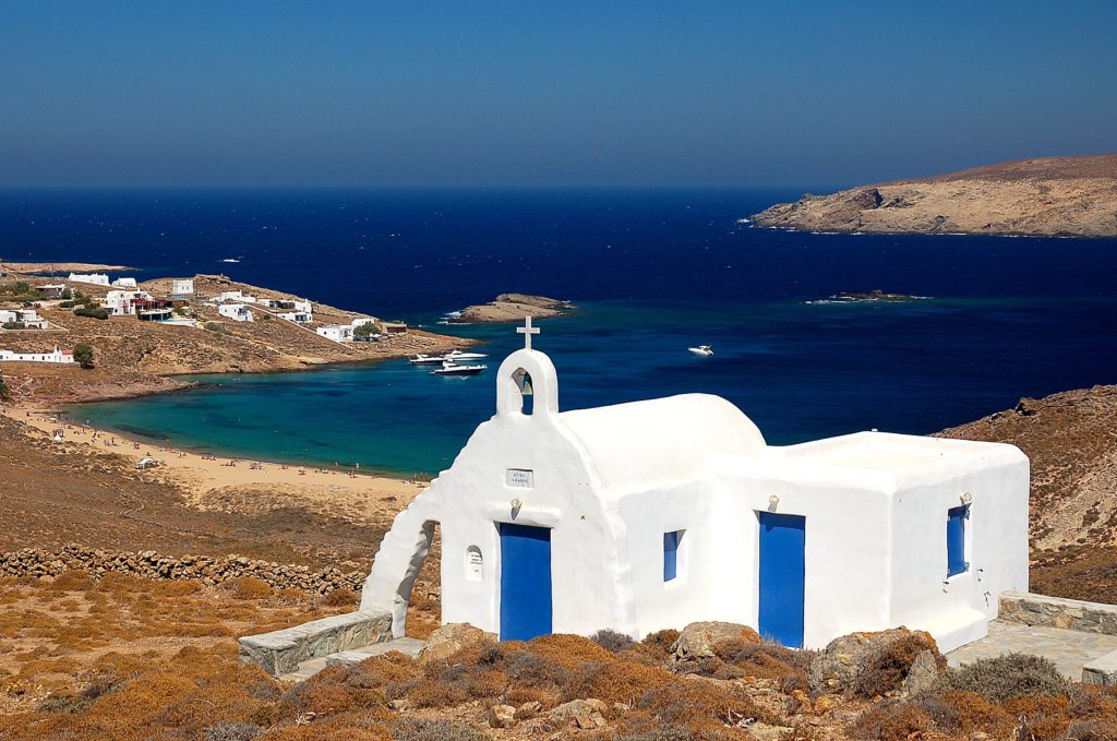 Belle chapelle blanche avec les portes bleues. en arrière plan une magnifique plage à l'eau cristalline. A faire à Mykonos