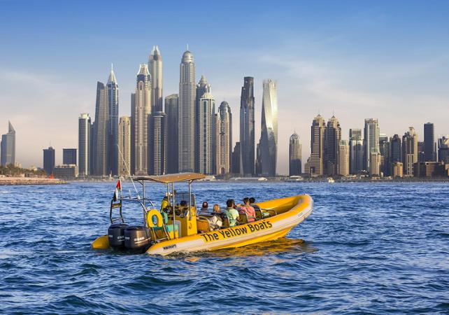 un zodiac jaune au milieu de l'eau promenant des visiteurs avec les buildings en arrière plan, une des activités à faire à Dubai.