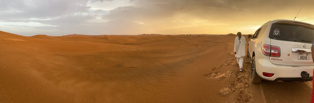 Un 4x4 au milieu du désert avec son conducteur qui marche à coté, une des activités à faire à Dubai.