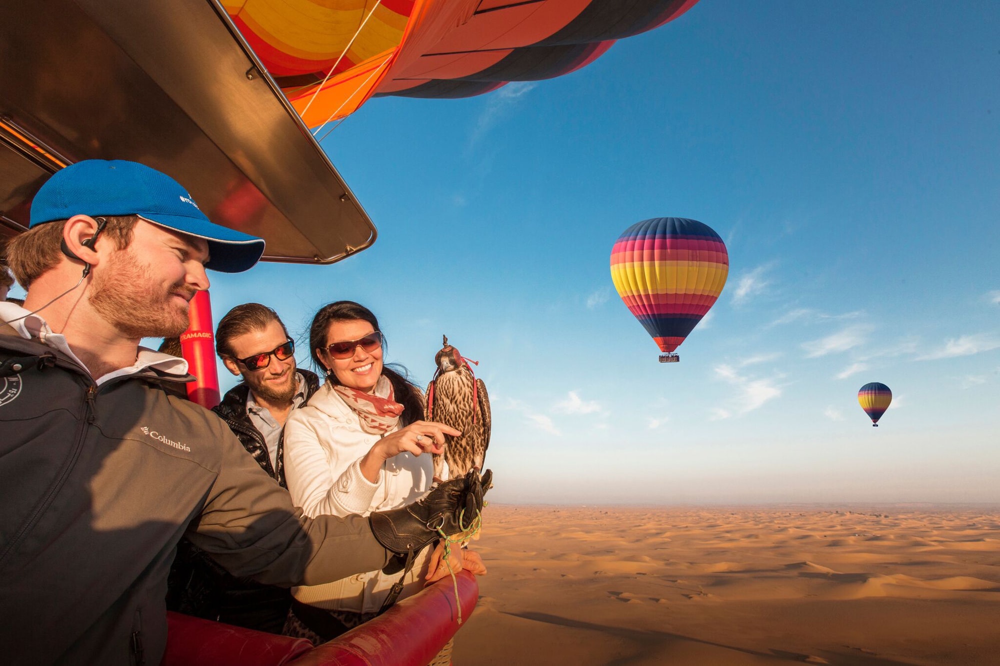3 personnes dans une montgolfière dans les air stenant un faucon. Deux autre montgolfières se voient au loin. C’est l’une des activités à faire à Dubai. 
