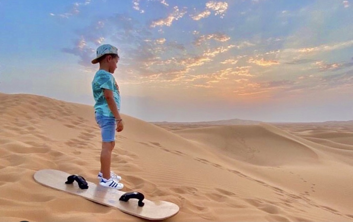 Une des activités à faire à Dubai, le snowboard sur le sable du désert. Sur la photo se tient un enfant avec son snow prêt à descendre de la dune.