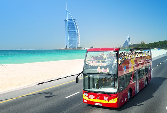 Bus à étage qui roule sur une route avec l'hôtel Burj Al Arab en arrière plan, une des activités à faire à Dubai
